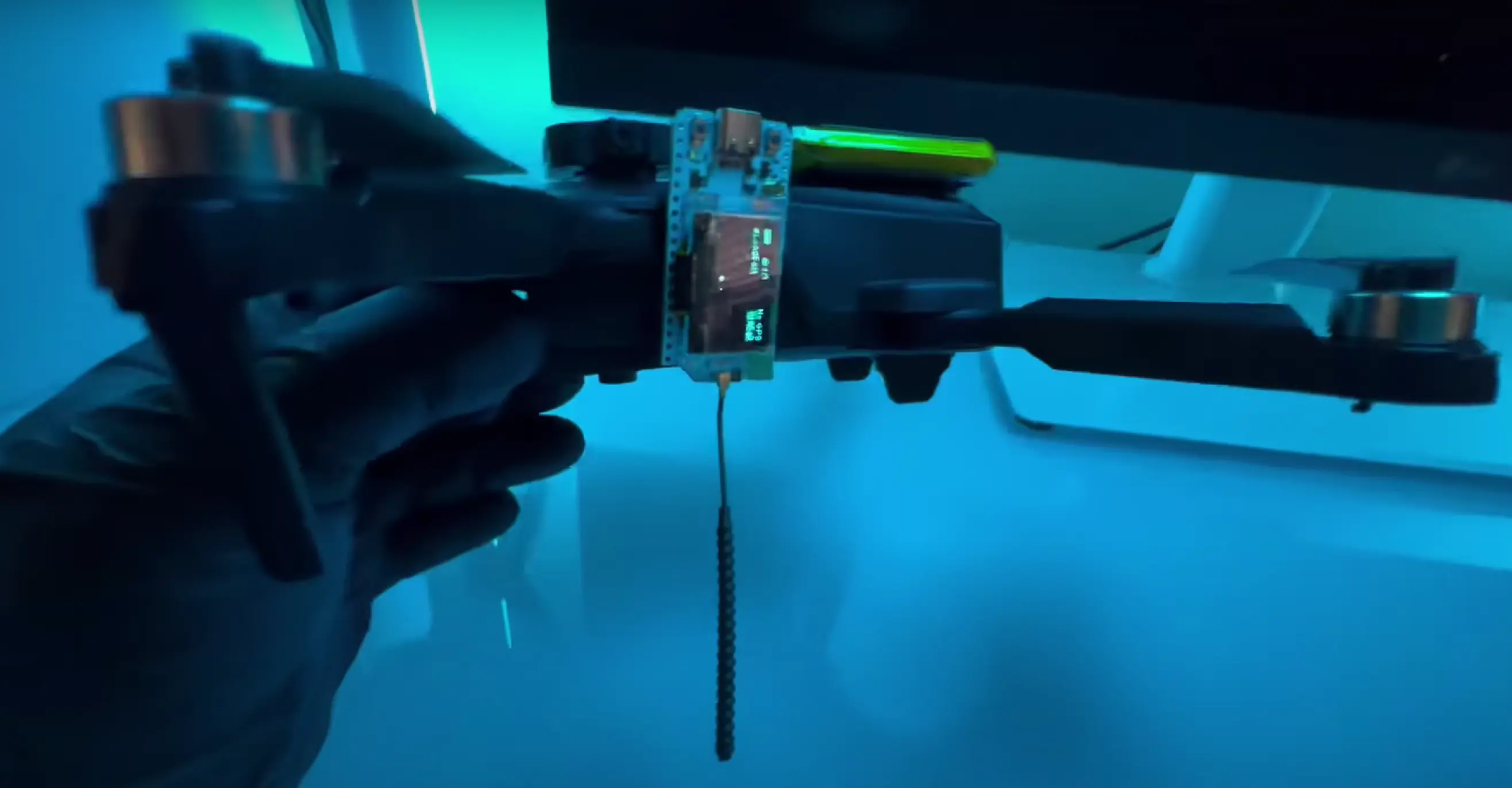 图片展示了一台无人机，其顶部安装了 Meshtastic 设备和电池。Meshtastic 设备固定在无人机的一侧，天线垂直向下，确保飞行过程中信号传输的最佳效果。这种设置演示了将 Meshtastic 设备与无人机结合，改造成移动通信基站的过程，为克服地形障碍和扩大通信范围提供了一种创新解决方案